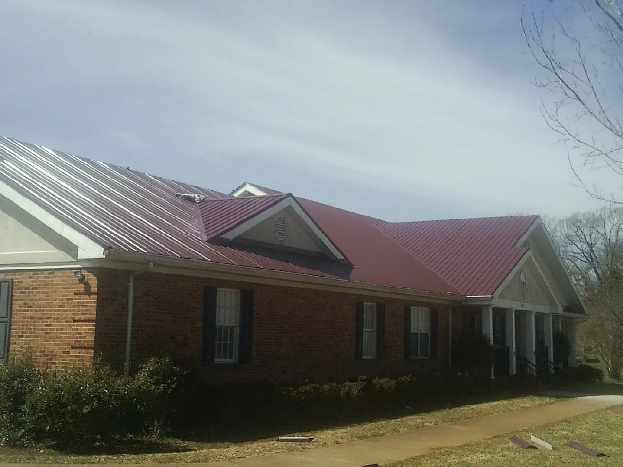 Red metal roof with gabled entries on a long brick building, from a Hail Damage Roof Repair job in Perry